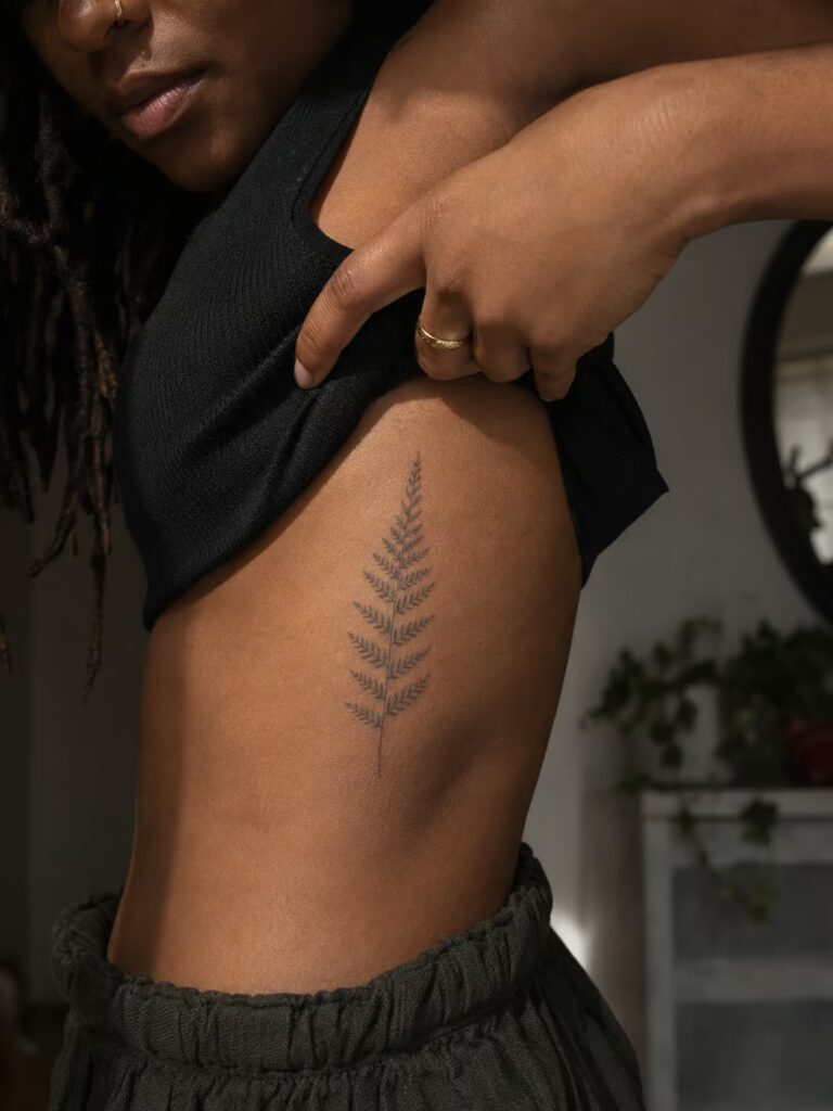 A fine fern frond along the rib cage for quiet endurance fine line tattoo