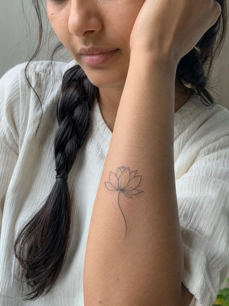A fine line tattoo of a lotus on the forearm for growth through hardship