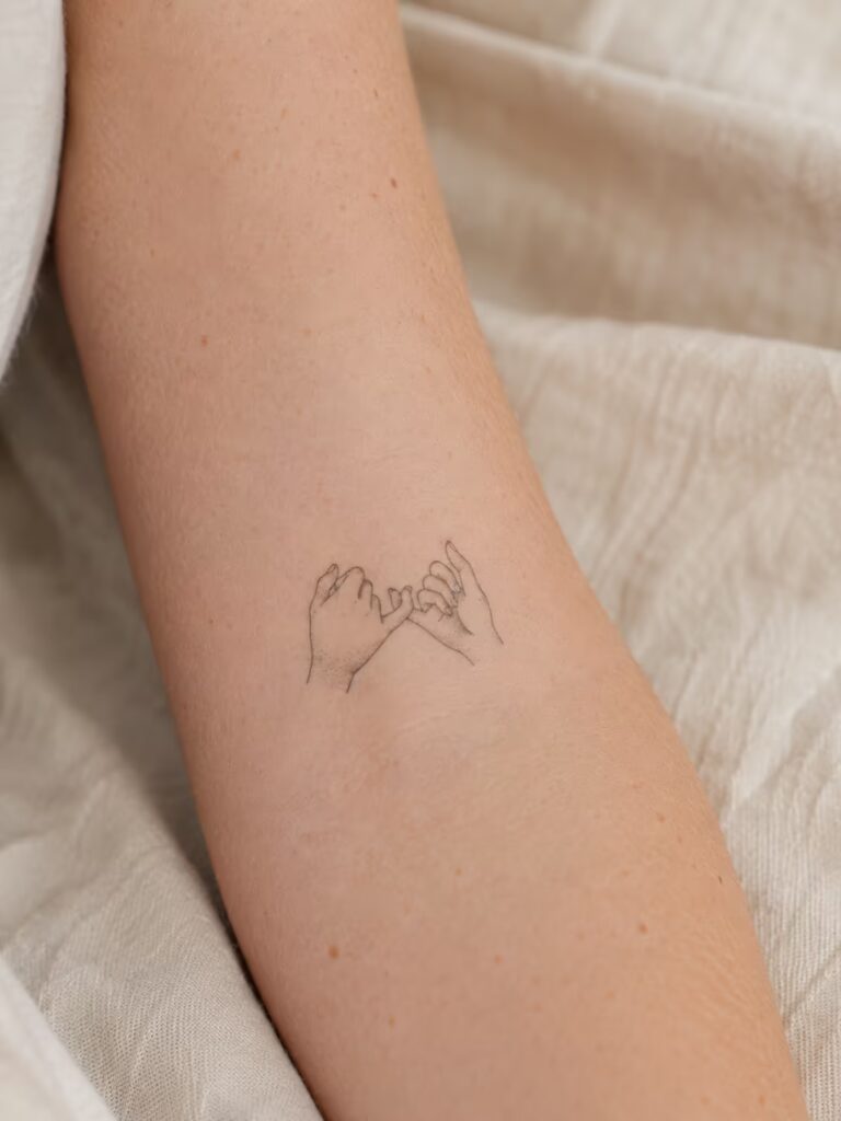 A Small Bestie Tattoo of Two Hands in a Pinky Promise on the Inner Forearm